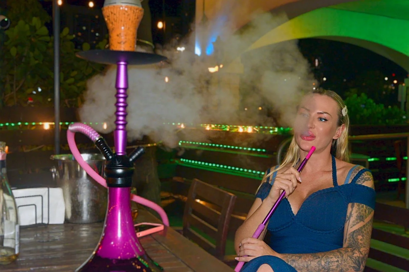 A guest exhaling smoke from a pink hookah on the patio